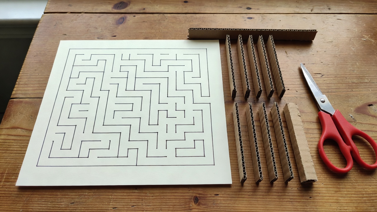 A drawn maze base and separate cardboard wall strips arranged beside scissors before assembly